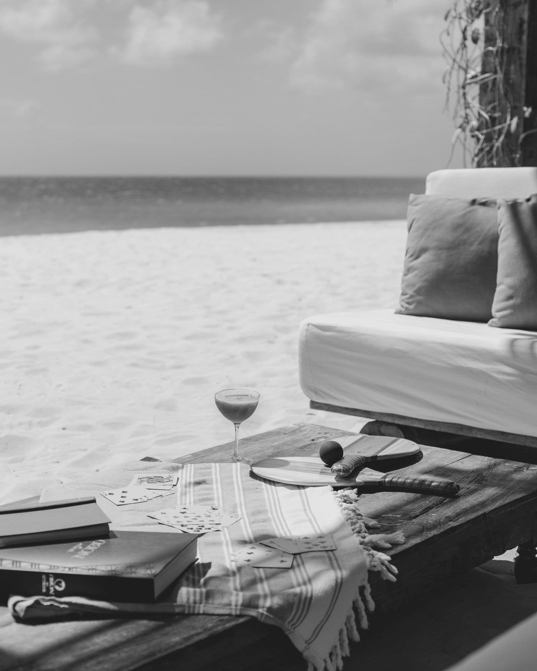 A beach daybed with a drink, cards and books on a low table